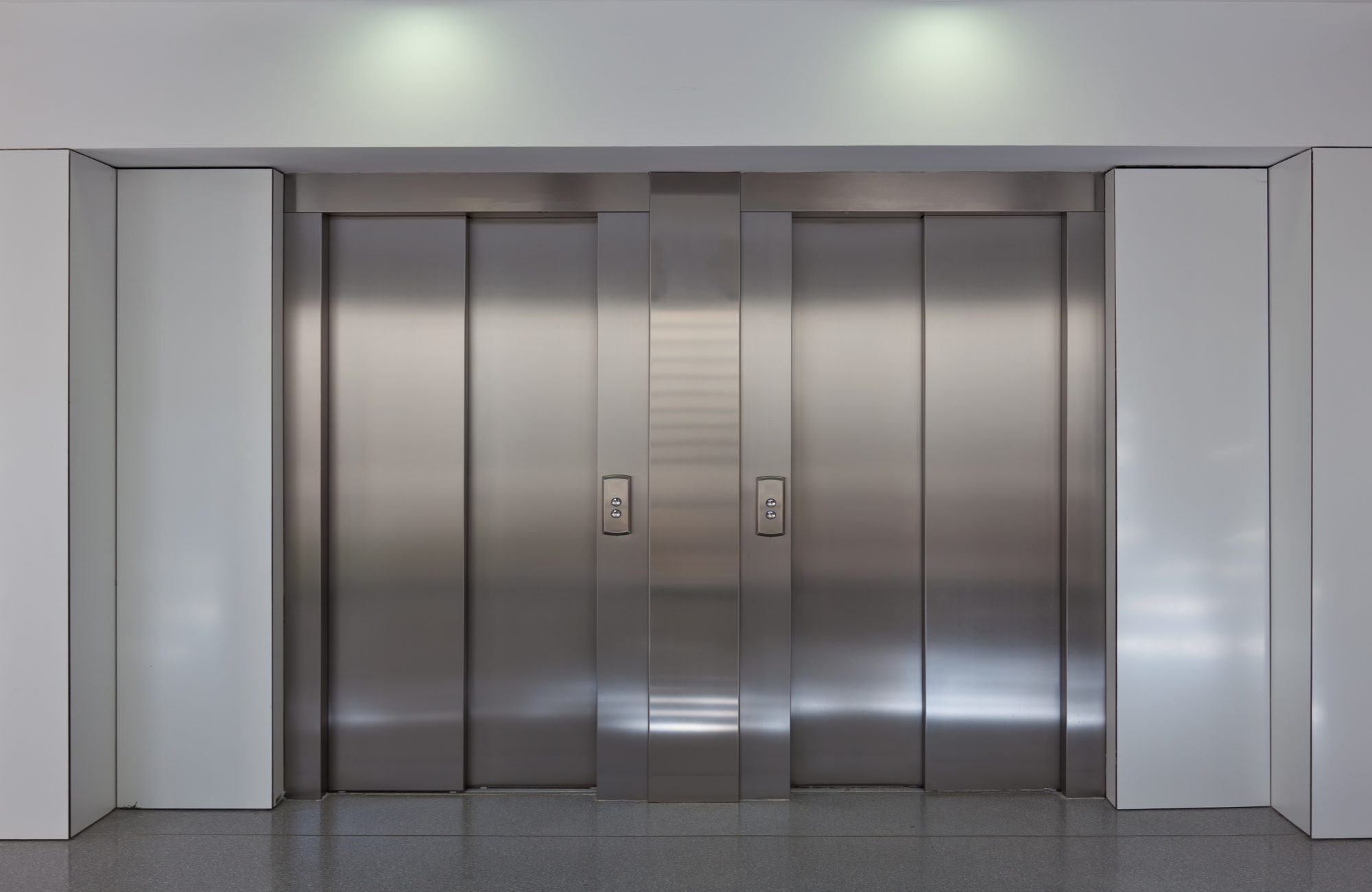 Two brushed metal elevator doors in a minimalistic style building interior